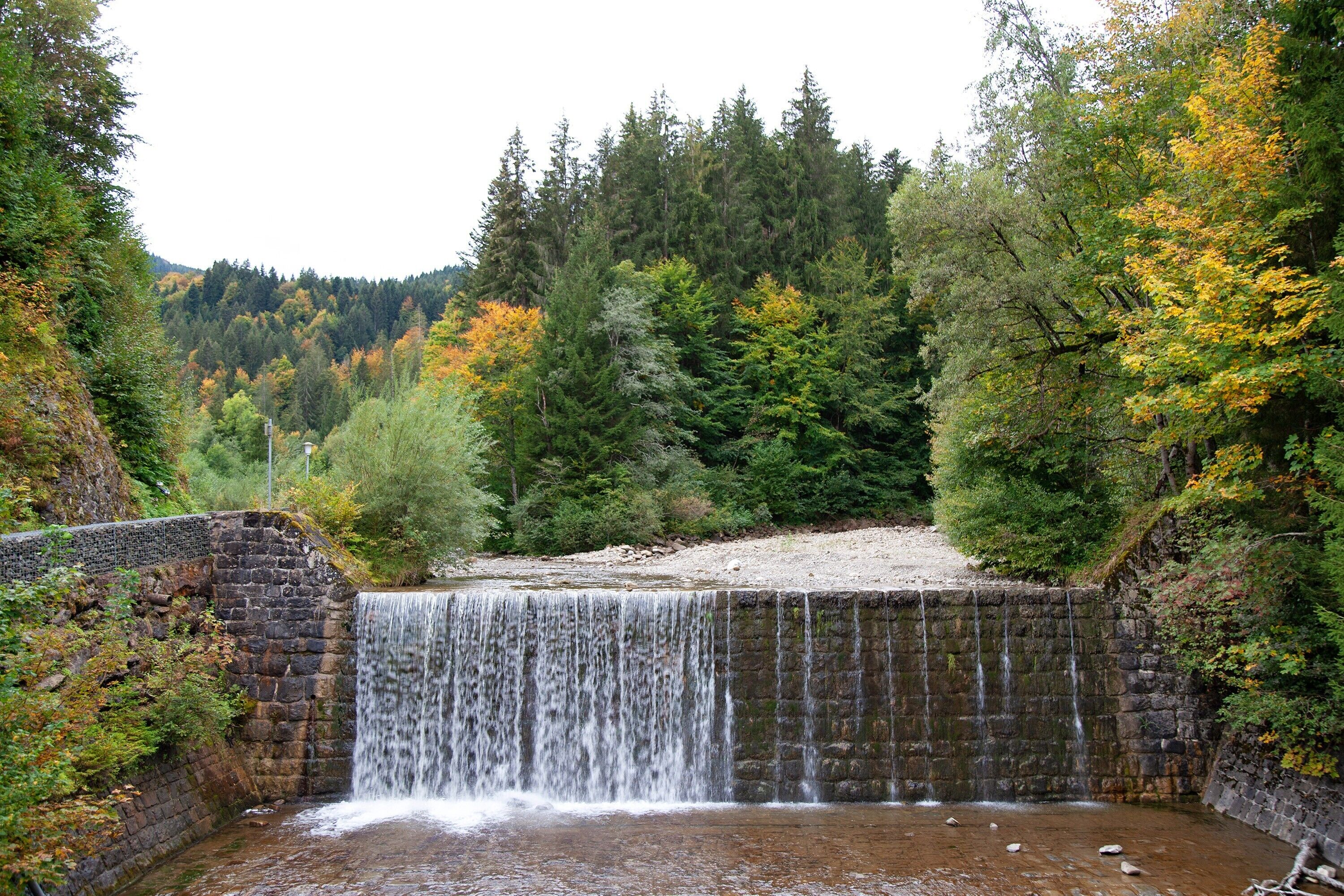 A waterfall cascading over a stone dam surrounded by dense forest.