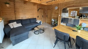 A cozy log cabin interior with a sofa, dining table, chairs, and a kitchen area. - Holiday Home 'Idylle Ferienhaus Ems' with Lake View, Wi-Fi and Air Conditioning (Walchum)