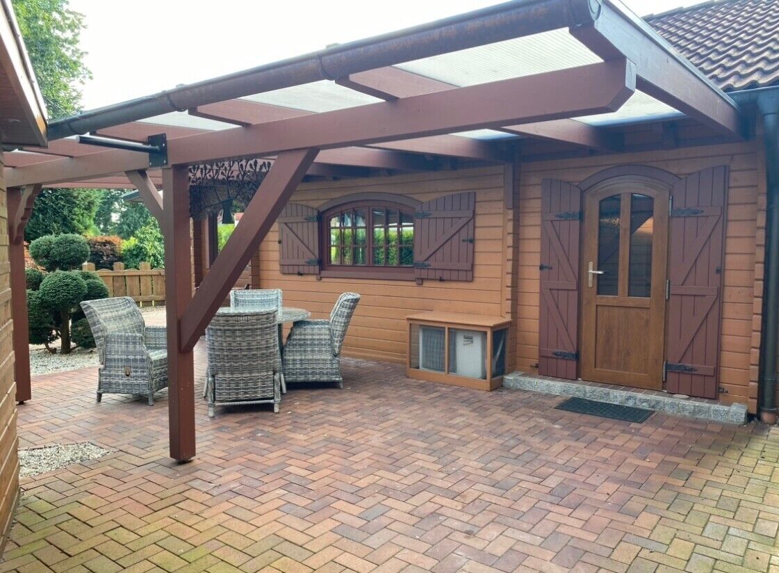 A covered patio with wicker furniture, a wooden door, and a brick floor.