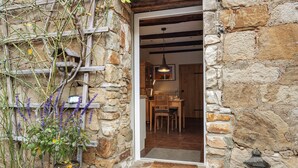 Pared exterior de piedra, una puerta de madera, zona de comedor con sillas y mesa, y una lámpara colgante.
