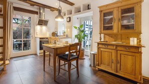 Una cocina con una mesa de madera, sillas, una lámpara colgante, un armario y una ventana.