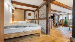 Un dormitorio con una cama de madera, pared de piedra, vigas de madera, un televisor y una planta.