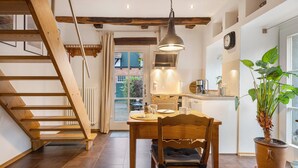 Una cocina con una escalera de madera, una mesa de comedor con sillas, una planta en maceta y una ventana.