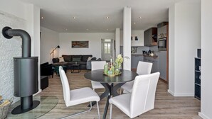 Una sala de estar moderna con una mesa redonda, sillas blancas, un sofá y una cocina al fondo.