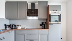 Una cocina moderna con armarios grises, encimera de madera, horno empotrado y cafetera.