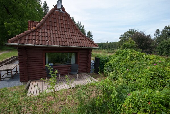 A log cabin with a tiled roof, a deck, and a window.
