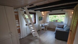 Quarto compacto com piso de madeira, um sofá, uma mesa e uma escada.