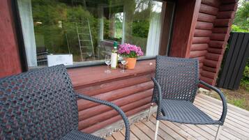 Eine Holzterrasse mit zwei Korbstühlen, einer Weinflasche und einem Blumentopf.