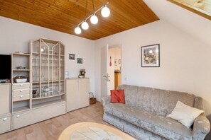 A living room with a sofa, a glass cabinet, a television, and a wooden ceiling.