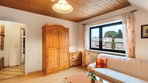 Una habitación con techo de madera, un armario grande, un sofá con vistas al exterior y una ventana con cortinas.