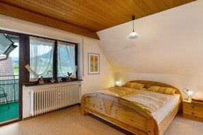 A bedroom with a wooden bed, a radiator, a window with curtains, a ceiling light, and a framed picture on the wall. - Apartment 'Ferienwohnung Hanna' with Mountain View, Balcony and Wi-Fi (Oberkirch)