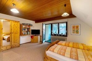 A bedroom with a wooden ceiling, a bed with patterned bedding, a television, a bookshelf, and a window with a view.