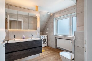 Een moderne badkamer met een grote spiegel, een wastafel, een wasmachine en een toilet.
