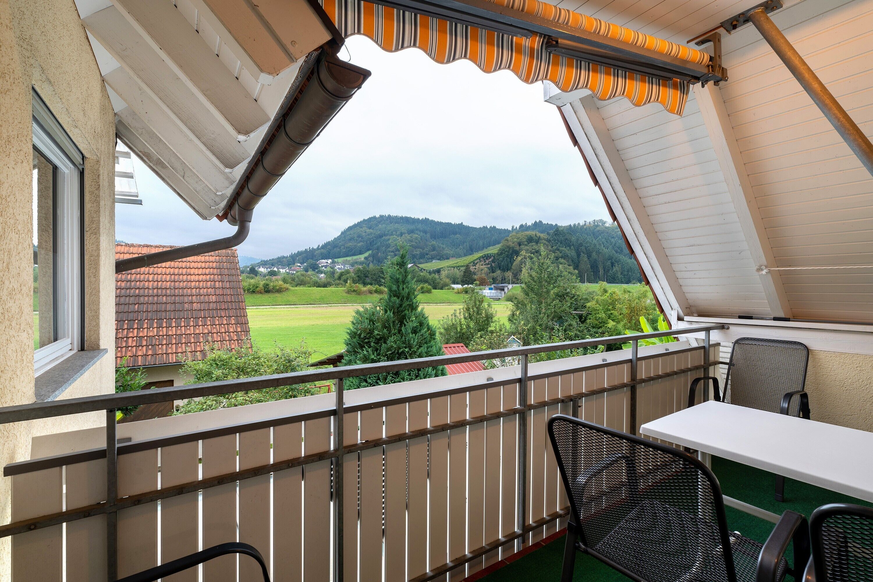 Ein Balkon mit Blick auf eine grüne Landschaft und Hügel, einem Tisch und zwei Stühlen.