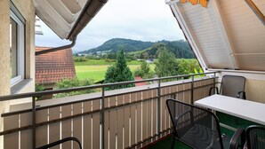Un balcón con vistas a un paisaje verde y colinas, una mesa y dos sillas.