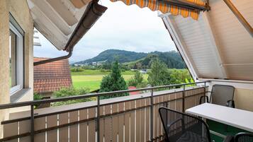 Ein Balkon mit Blick auf eine grüne Landschaft und Hügel, einem Tisch und zwei Stühlen.