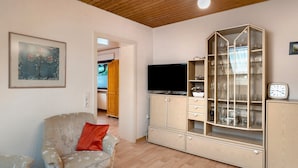 Una sala de estar con televisor, un mueble con puertas de vidrio y una silla.