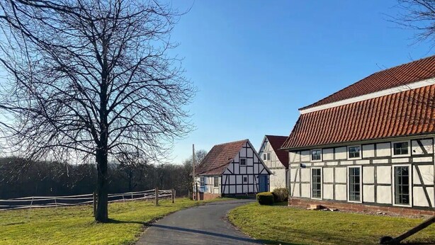 Camino rural que lleva a casas tradicionales con entramado de madera bajo un cielo despejado.