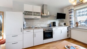 A modern kitchen with white cabinets, a built-in oven, a microwave, and a window with curtains. - Apartment 'Haus Sünnschien' with Shared Terrace, Shared Garden and Wi-Fi (Nordstrand)