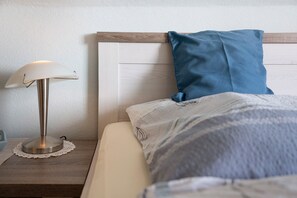 Un lit bien fait, avec un oreiller bleu, une lampe de chevet et une tête de lit en bois.