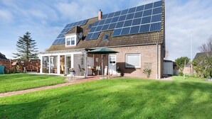 A house with solar panels on the roof, a covered patio, and a well-maintained lawn. - Apartment 'Haus Sünnschien' with Shared Terrace, Shared Garden and Wi-Fi (Nordstrand)