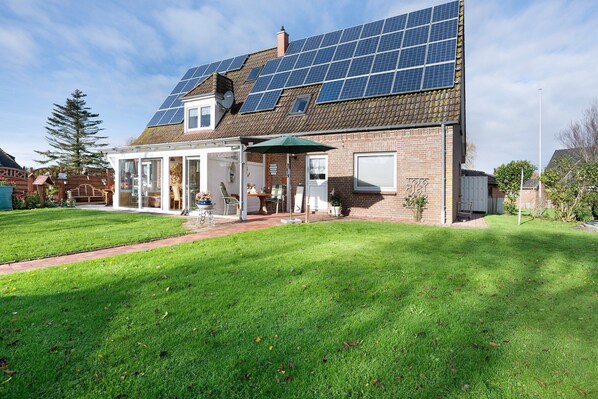 Une maison dotée de panneaux solaires sur le toit, d’un patio abrité et d’une pelouse bien entretenue.