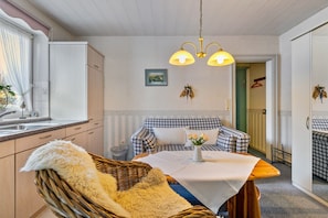 Ein gemütliches Zimmer mit einem karierten Sofa, einem Korbstuhl, einem Esstisch mit einer Vase und einer Pendelleuchte.