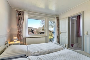 Ein Schlafzimmer mit zwei Betten, einem Fenster, einem Heizkörper und einer Tür zu einem Badezimmer.