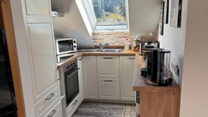 Une cuisine compacte avec des meubles blancs, un four encastré, un four à micro-ondes, un évier et une fenêtre située au-dessus de l’évier.