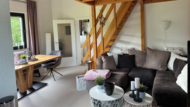 Un salon moderne avec un plafond en bois, un ensemble de canapés, une table à manger et un escalier.