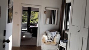 Un couloir avec un plancher en bois, une chaise blanche avec un coussin moelleux, une petite table et une armoire.