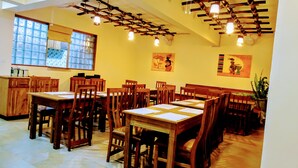 A dining area with wooden tables and chairs, ceiling fans, and artwork on the walls. - SERENITY FORT HOTEL (Mariakani)