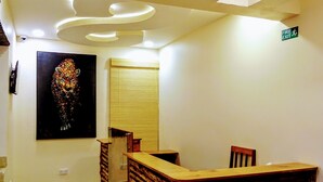 A reception desk with a wooden design, a painting on the wall, and a fire exit sign. - SERENITY FORT HOTEL (Mariakani)