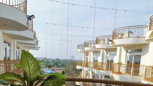 A balcony with a potted plant, a view of a street, and a multi-story building with balconies. - SERENITY FORT HOTEL (Mariakani)