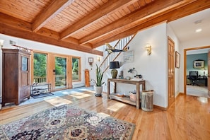 A spacious living room with a wooden ceiling, a staircase, and a large rug.