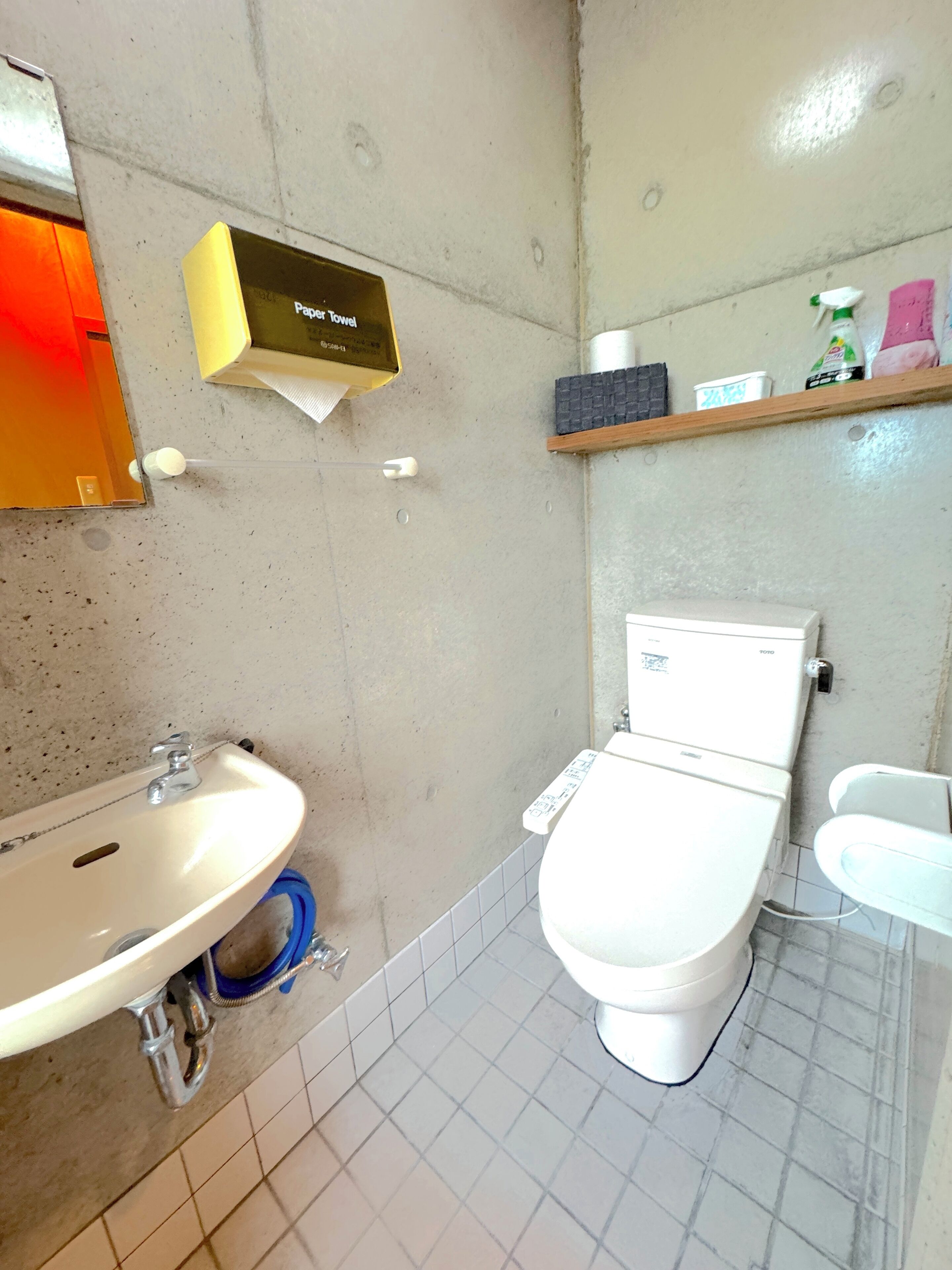 A bathroom with a white sink, toilet, and a shelf with toiletries.
