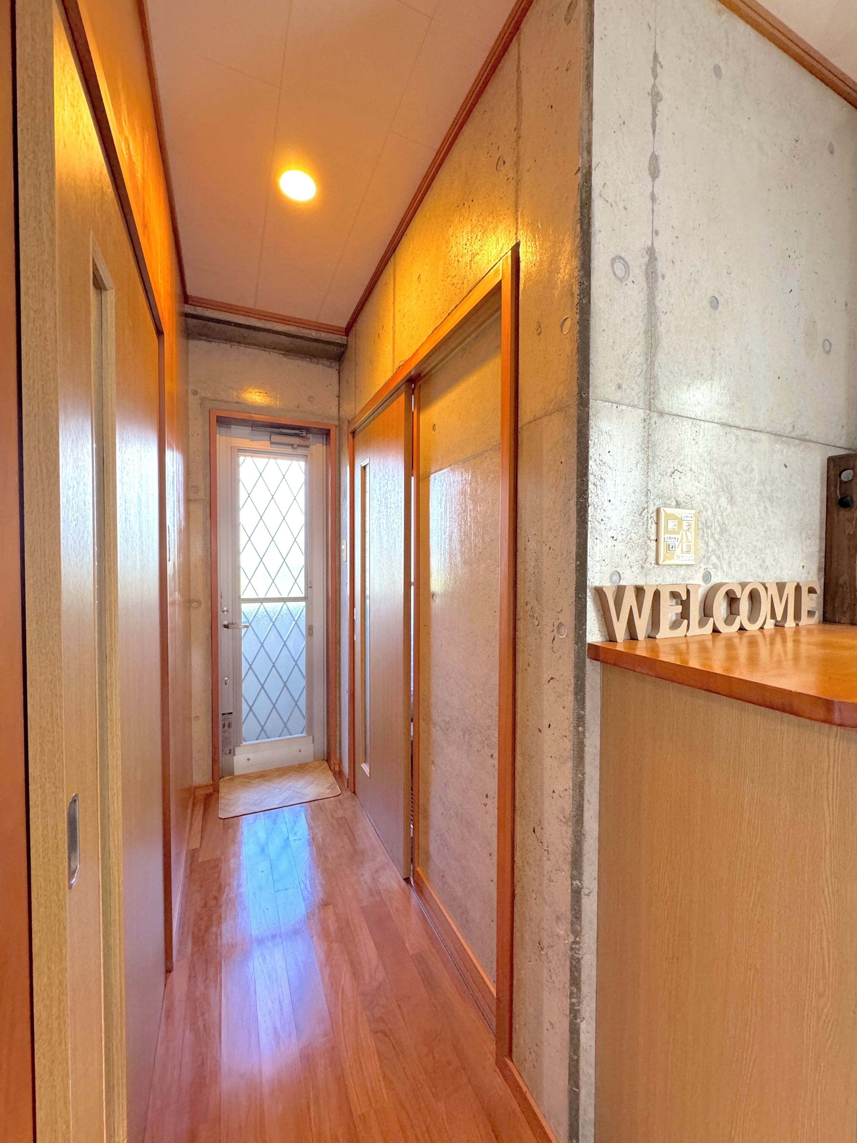 A hallway with wooden flooring, a reception desk with a 'WELCOME' sign, and a door with a frosted glass window.