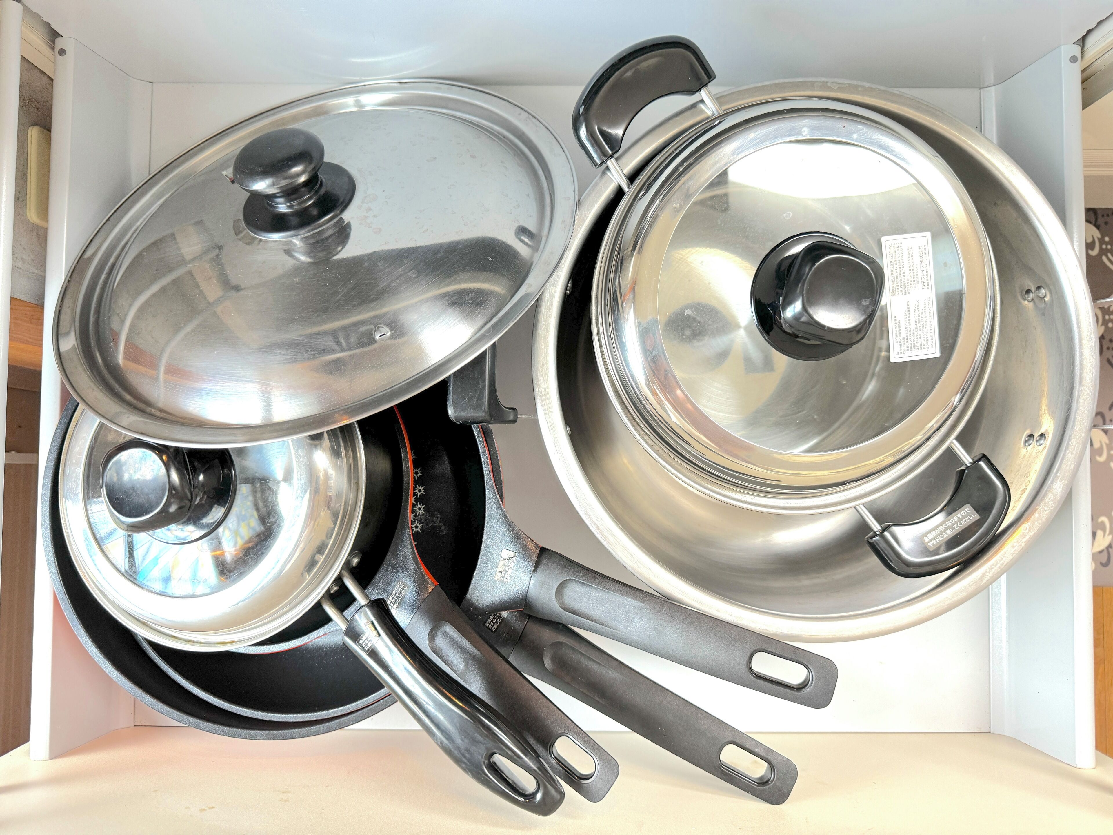 A kitchen with two stainless steel pots with lids, a black pan, and a black pot with a handle.