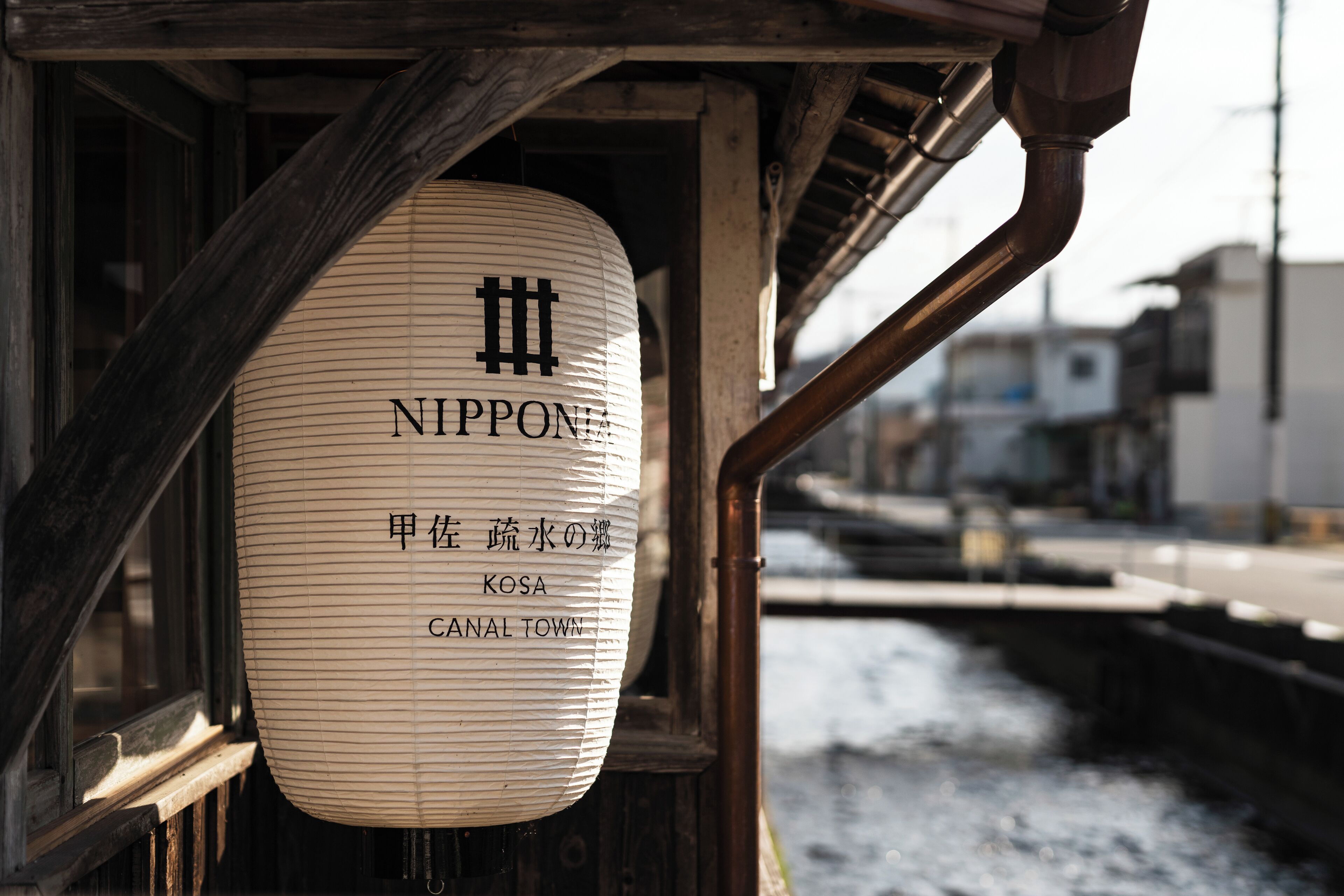 Un farol tradicional japonés con texto, suspendido cerca de una estructura de madera junto a un canal.