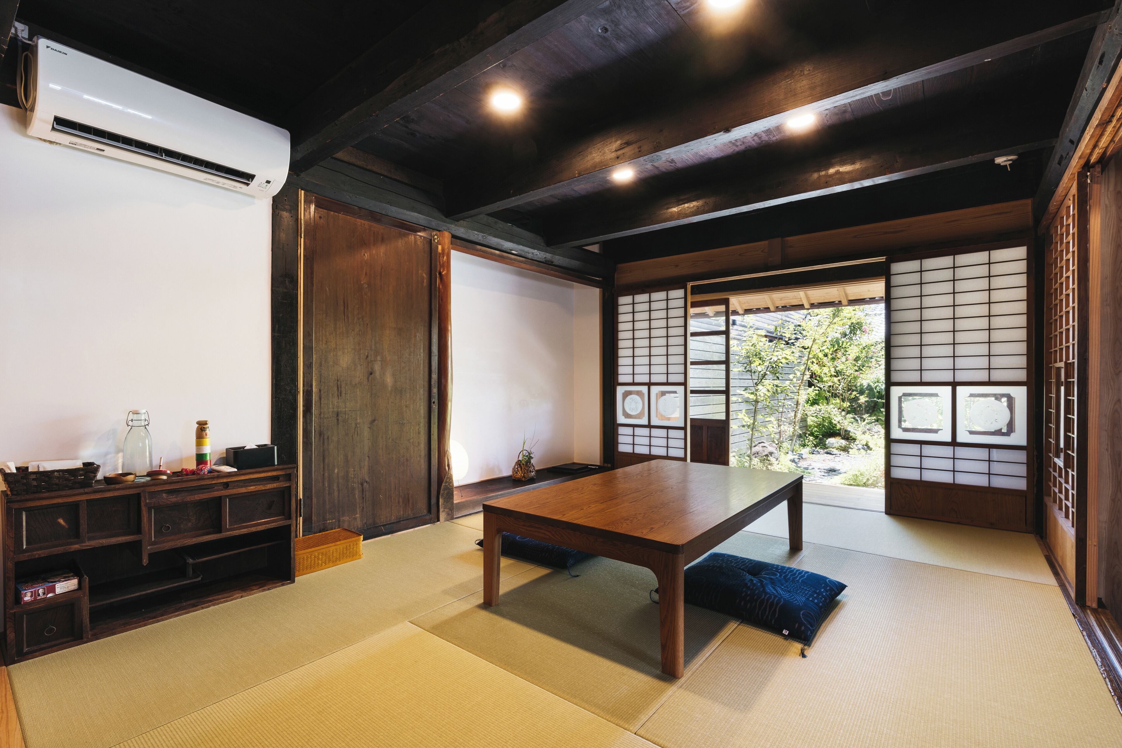 A traditional Japanese room with tatami flooring, a wooden table, a low cabinet, and sliding doors with a view of greenery outside.