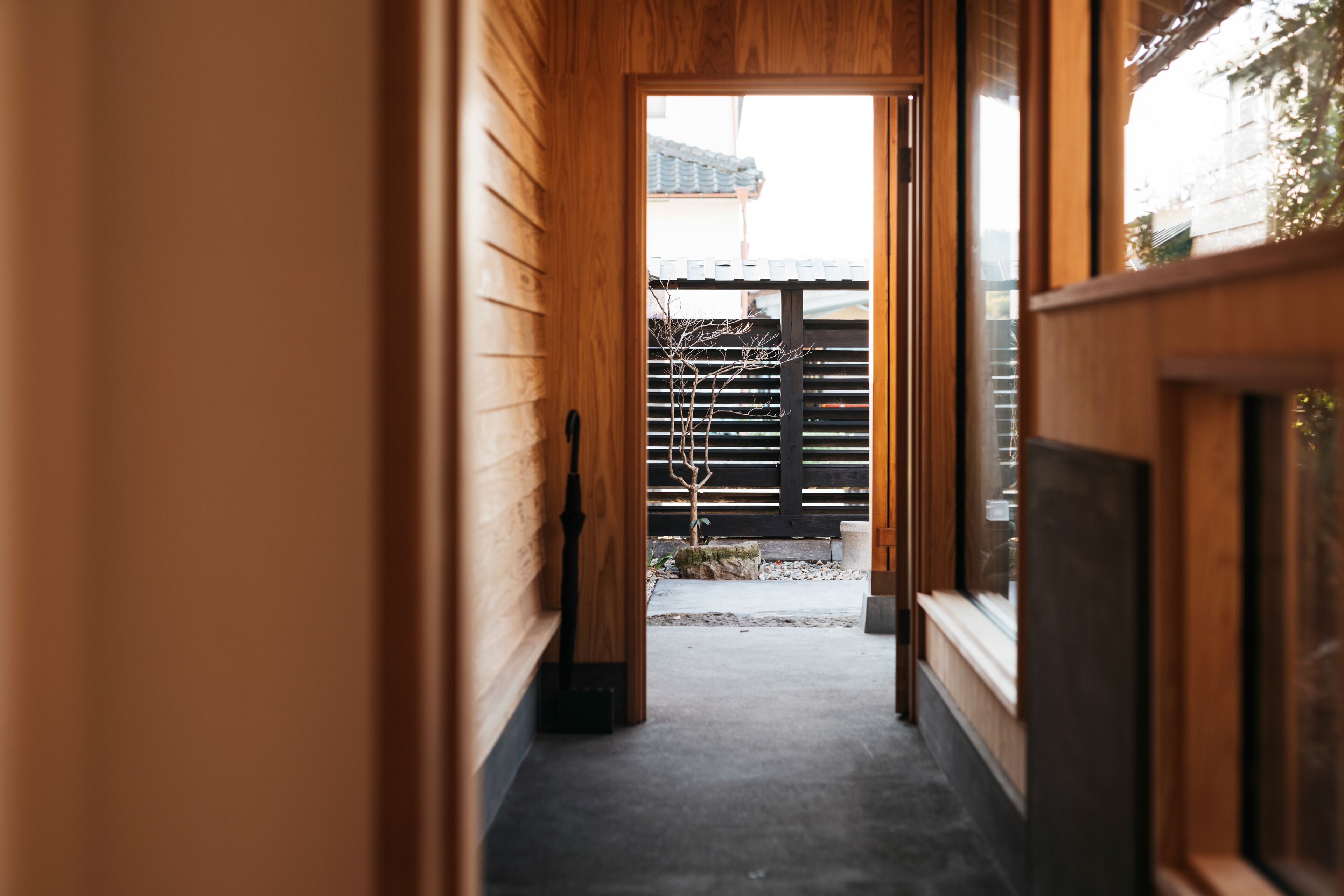A wooden interior hallway leading to an outdoor area with a wooden fence and a small tree.