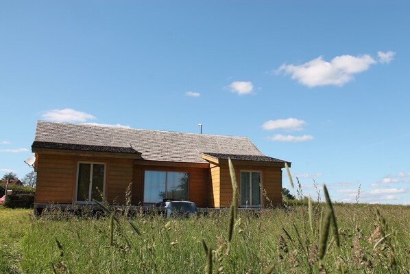 A wooden house with a sloped roof, large windows, and a satellite dish.