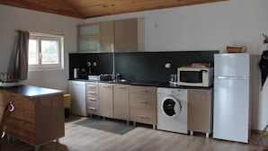 A compact kitchen with wooden cabinets, a washing machine, a microwave, and a refrigerator. - Une Maison en Bois du Québec Près de Nevers, Moulins, le Pal et les Canaux ! (Saint-Germain-Chassenay)