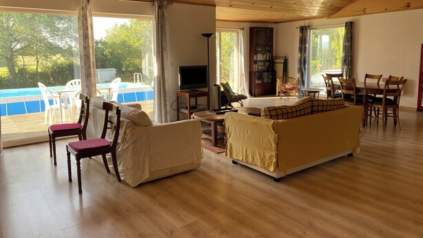 A spacious living room with a wooden ceiling, large windows, a pool, and a dining area. - Une Maison en Bois du Québec Près de Nevers, Moulins, le Pal et les Canaux ! (Saint-Germain-Chassenay)
