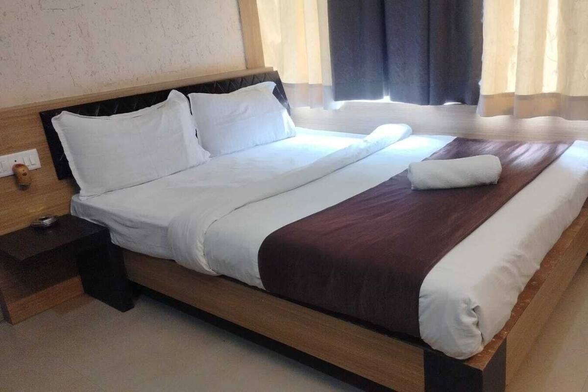 Uma cama bem arrumada com lençóis brancos e castanhos, uma cabeceira de madeira e uma mesa de cabeceira com um abajur.