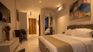 A modern hotel room with a large bed, a desk with chairs, a mirror, and a painting on the wall. - Oasis Retreat at 233 Boulevard (Accra)
