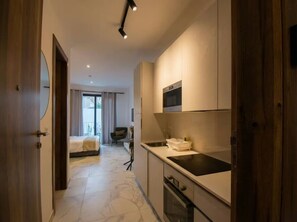 Een moderne keuken met een inbouwoven en magnetron, een eethoek met een tafel en stoelen, en een slaapkamer met een bed en uitzicht op het omliggende landschap.