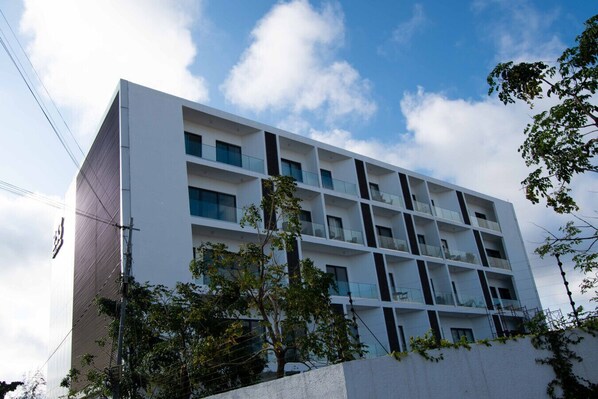 Un edificio moderno de varios pisos con fachada blanca, varios balcones y cielo despejado.