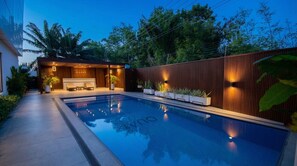 Una piscina con muelle de madera, zona de estar techada y valla de madera.