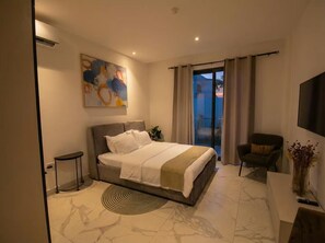 Een moderne slaapkamer met een groot bed, een klein nachtkastje, een stoel, een televisie en een schilderij aan de muur.